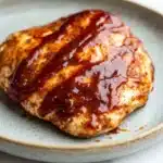 Air fryer chicken breast bbq - the image shows a plate with a piece of grilled chicken on it. the chicken is golden brown and appears to be seasoned with herbs and spices. it is covered in a thick, red sauce that is dripping down the sides of the chicken. the sauce is thick and thick, and it looks like it has been cooked to perfection. the plate is light blue and has a textured surface. the background is white, making the plate and chicken the focal point of the image.