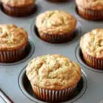 Banana muffin pictures - the image shows a muffin tin filled with freshly baked muffins. the muffins are golden brown in color and have a crumbly texture on top. they are arranged in a circular pattern in the tin, with each muffin slightly overlapping the one below it. the tin is sitting on a wooden countertop, and the background is blurred, but it appears to be a kitchen countertop.