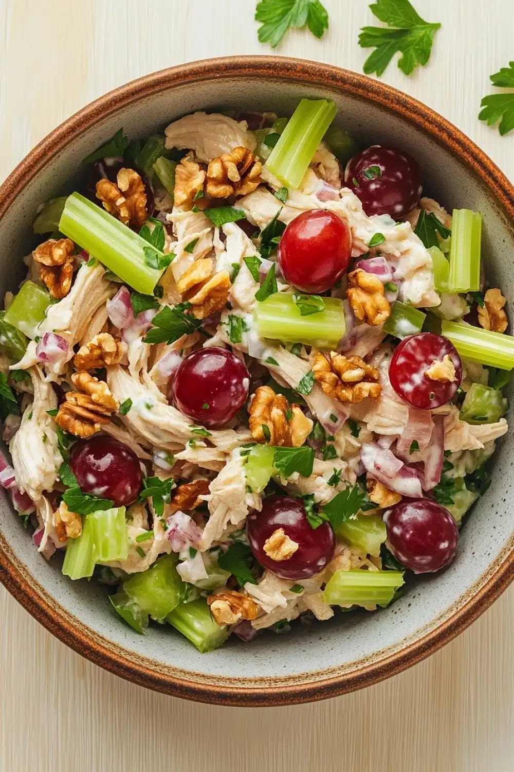 Chicken salad no mayo greek yogurt - the image is a close-up of a bowl of salad. the salad is made up of various ingredients, including chicken, celery, red onions, and walnuts. the chicken is cooked to a golden brown color and appears to be seasoned with herbs and spices. the celery is cut into thin strips and is scattered throughout the salad, while the red onions are sliced into small pieces. the walnuts are scattered throughout, adding a crunchy texture to the dish. there are also a few sprigs of parsley scattered around the bowl. the bowl is sitting on a light-colored wooden table.