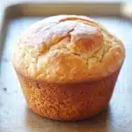 Muffin allo yogurt friggitrice ad aria - the image shows a freshly baked muffin on a baking tray. the muffin is golden brown in color and has a soft, fluffy texture. it appears to be freshly baked and is sitting on a wooden surface. the tray is lined with parchment paper and there is a window in the background, letting in natural light. the overall mood of the image is warm and inviting.