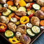 Sheet pan hibachi chicken and vegetables - the image shows a baking tray filled with grilled chicken and vegetables. the chicken is golden brown and appears to be seasoned with herbs and spices. the vegetables are sliced zucchini, bell peppers, and carrots. the tray is lined with parchment paper and is placed on a dark grey countertop. the colors of the vegetables are vibrant and the dish looks appetizing.